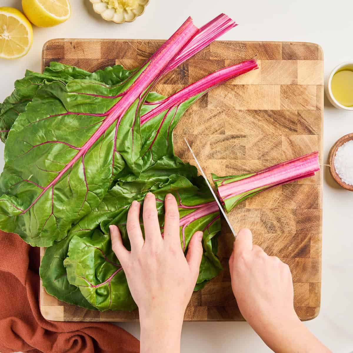 Woman slicing the stem from a leaf of red Swiss chard on a cutting board.