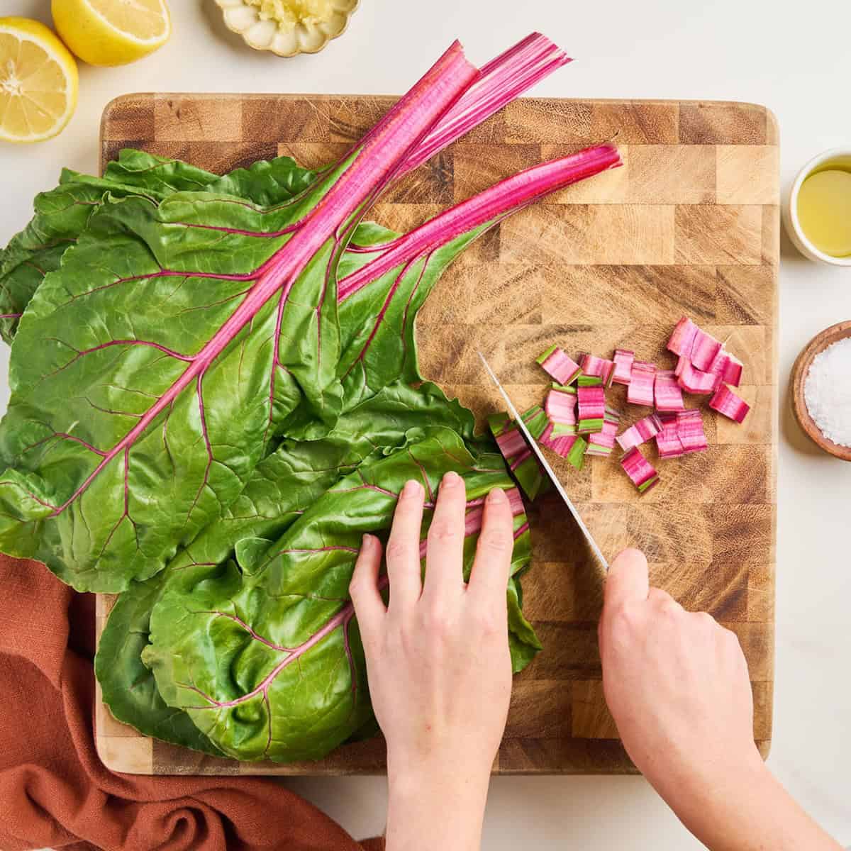 Woman slicing a red chard stem into small pieces on a cutting board.