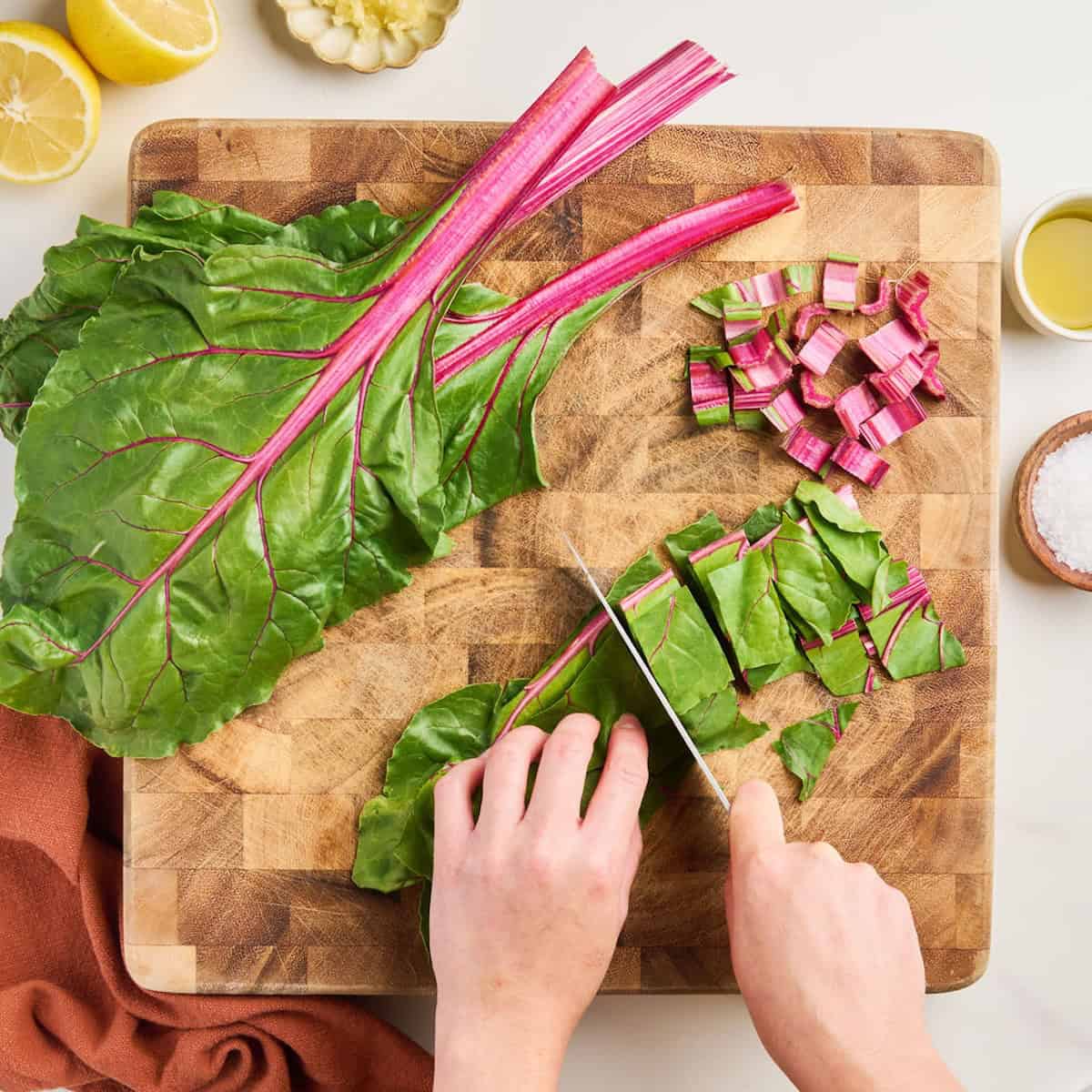 Woman roughly chopping red chard leaves with a knife on a cutting board.