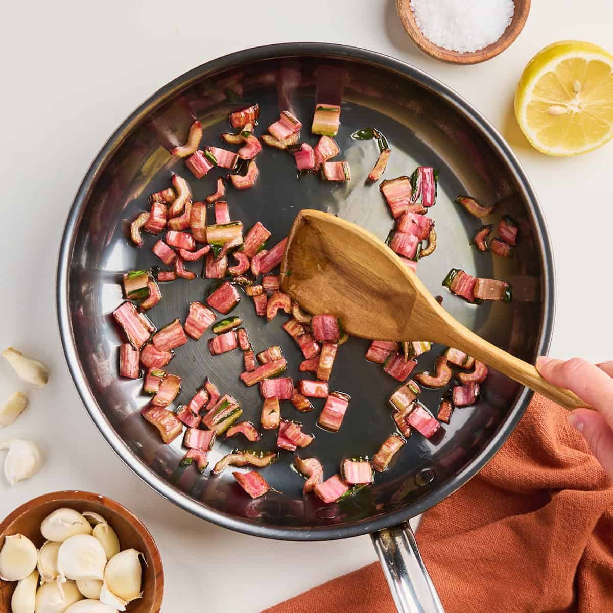 Woman stirring sautéed red chard stems with a wooden spoon in a skillet.