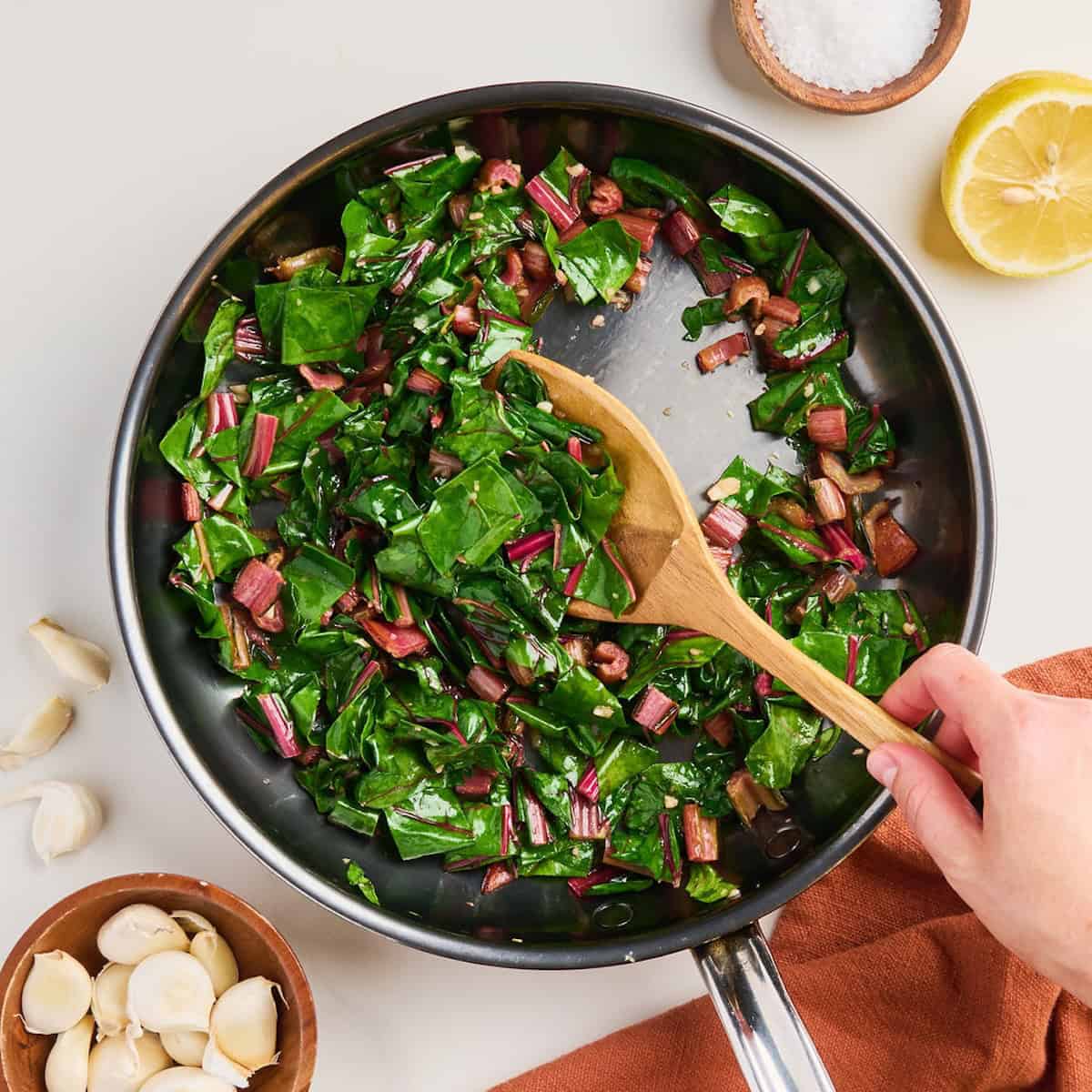 Woman stirring cooked red chard with a wooden spoon in a skillet.