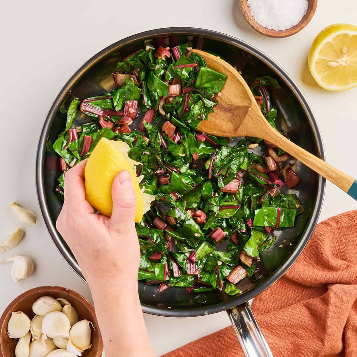 Woman squeezing lemon juice over garlicky Swiss chard in a skillet with a spoon.