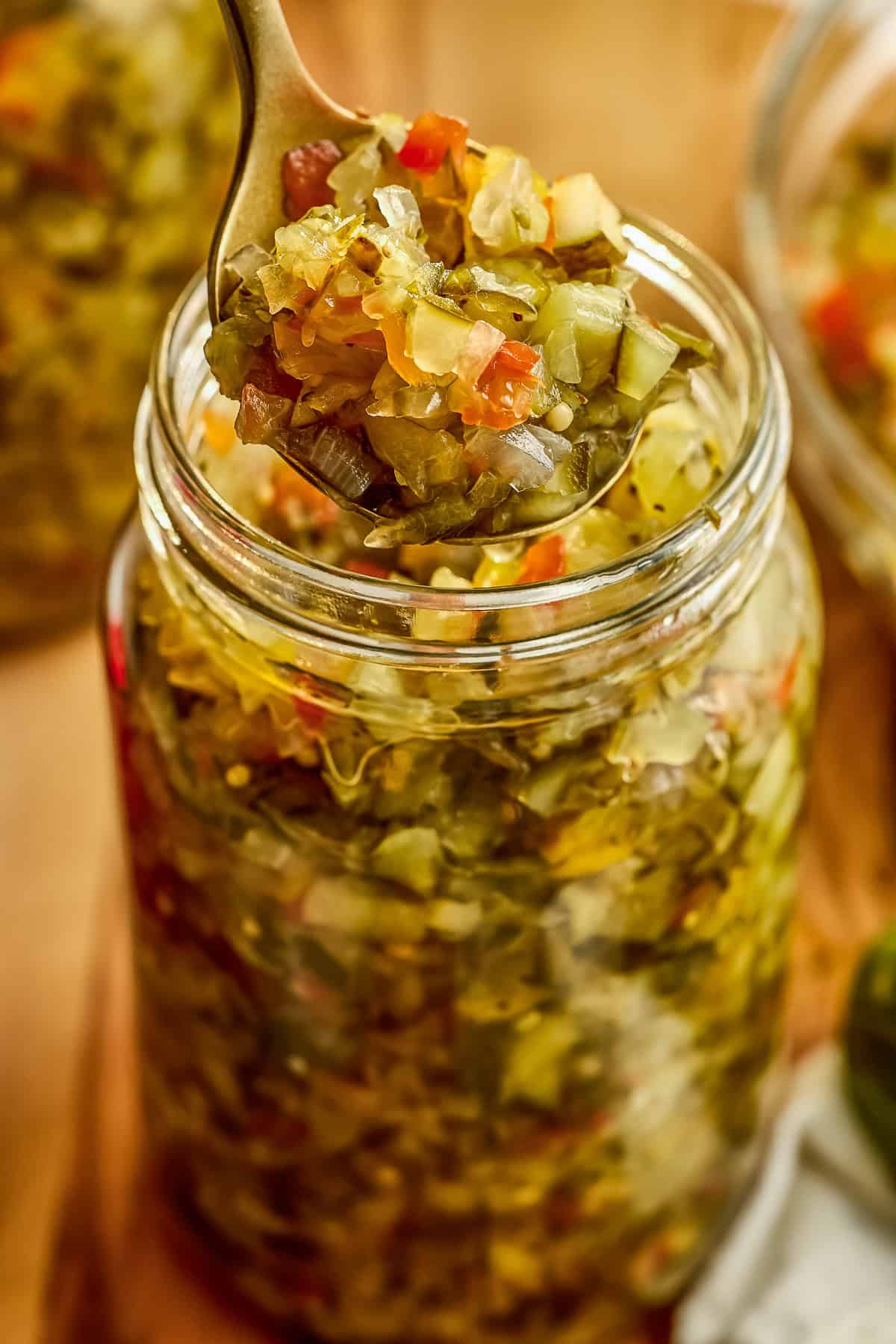 Homemade sweet relish recipe on a spoon being lifted out of a glass jar.