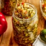 Homemade sweet relish recipe on a spoon being lifted out of a glass jar.