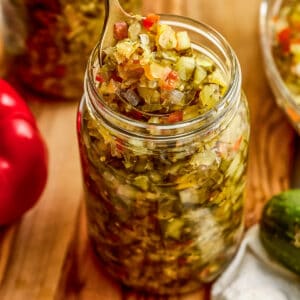 Homemade sweet relish recipe on a spoon being lifted out of a glass jar.