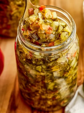 Homemade sweet relish recipe on a spoon being lifted out of a glass jar.
