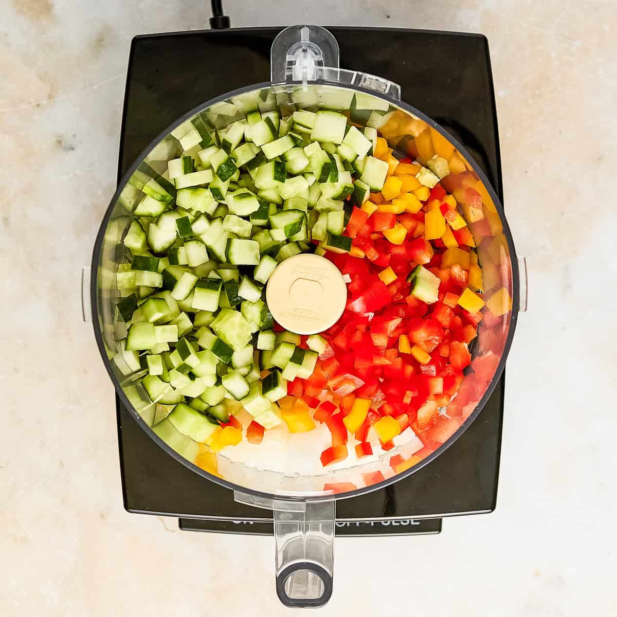 Cucumbers, bell peppers, and onion in a food processor to be chopped for relish.