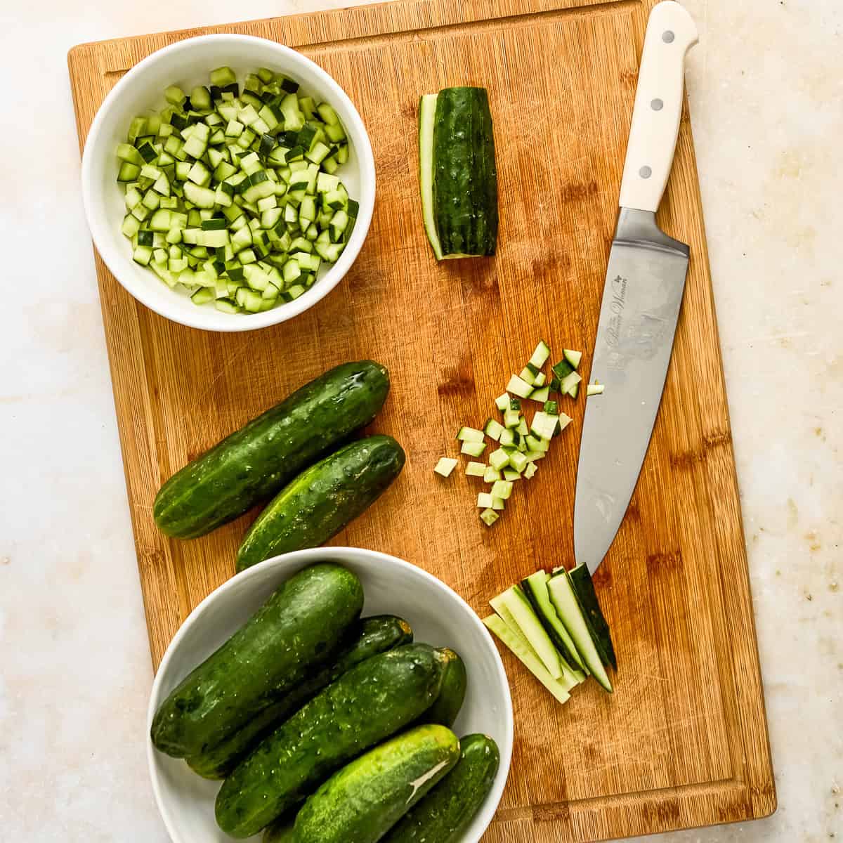 Pickling cucumbers chopped into small pieces on a wooden cutting board with a knife.