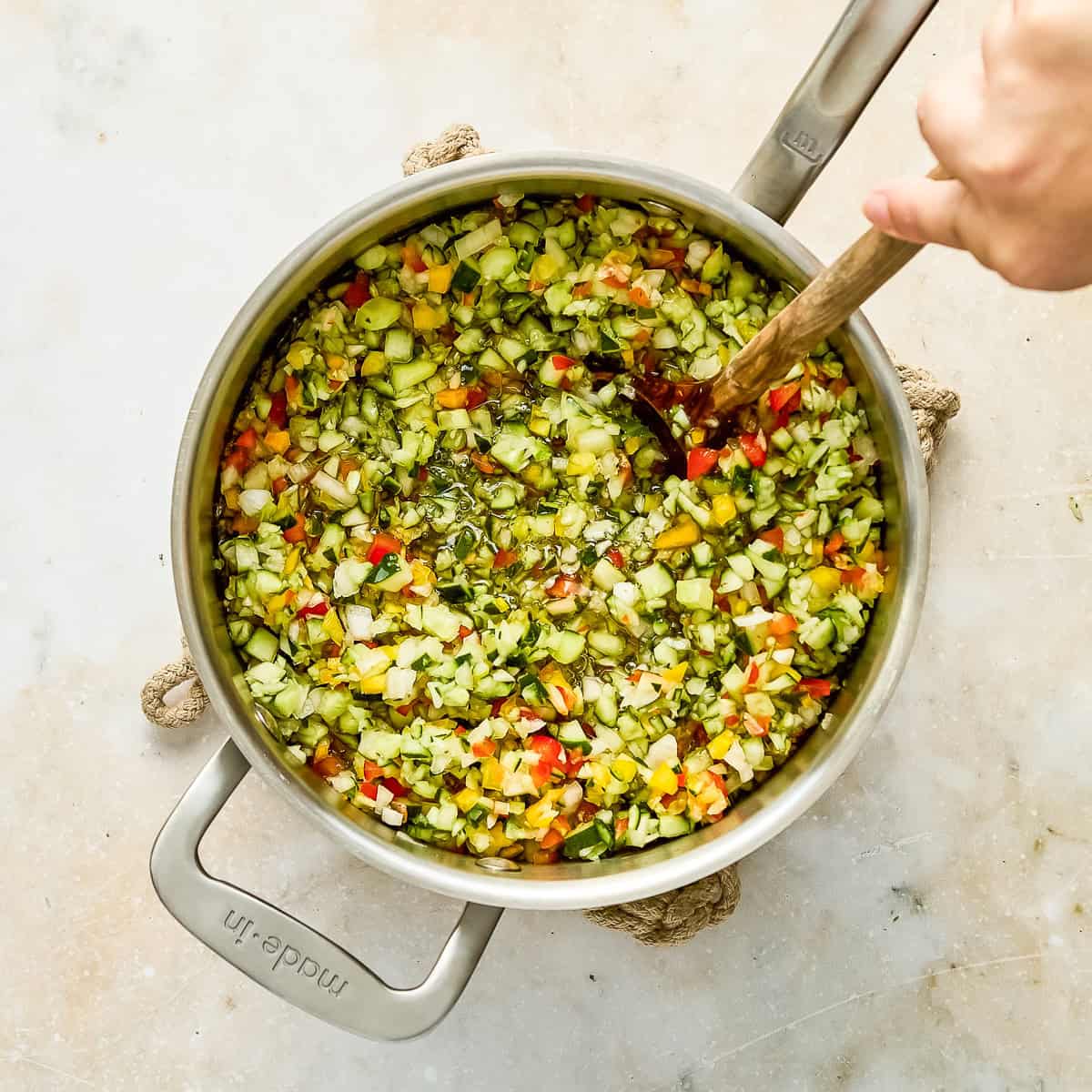 Woman stirring relish ingredients simmering in apple cider vinegar brine on a stovetop.