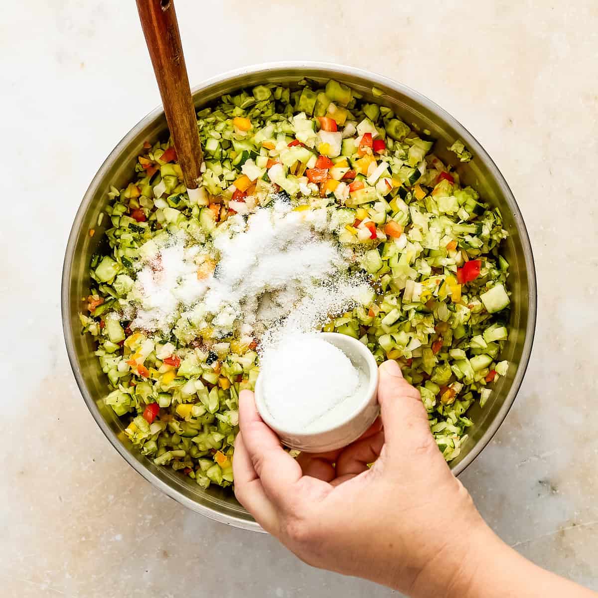 Woman sprinkling kosher salt into a bowl of sweet relish ingredients with a spoon.
