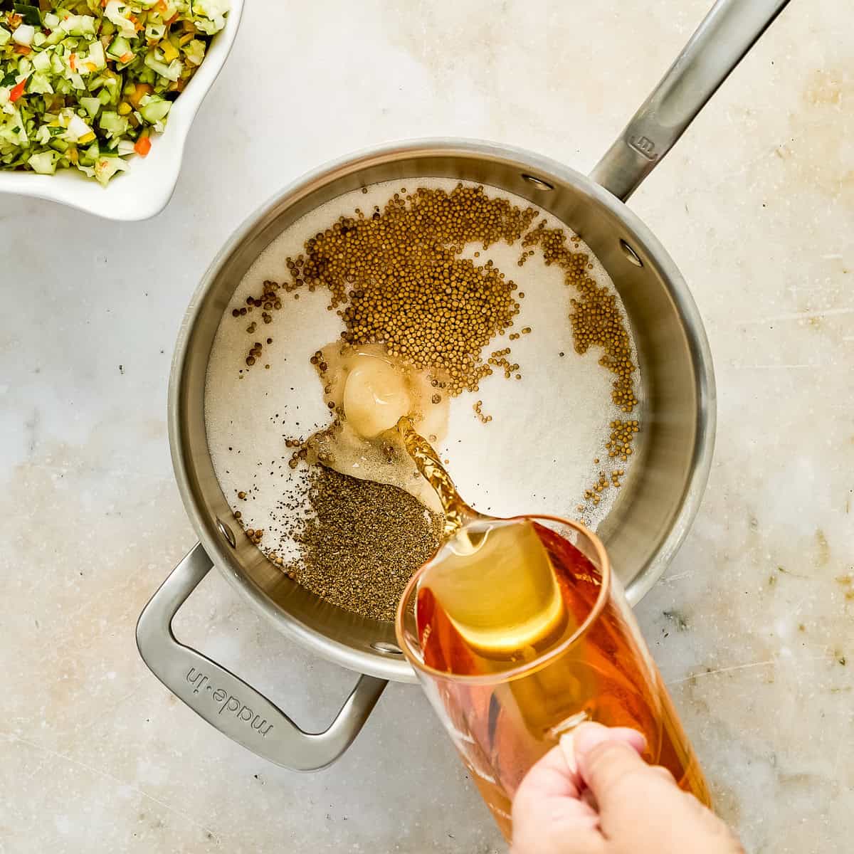 Woman pouring apple cider vinegar into a pot with sugar and seasonings.