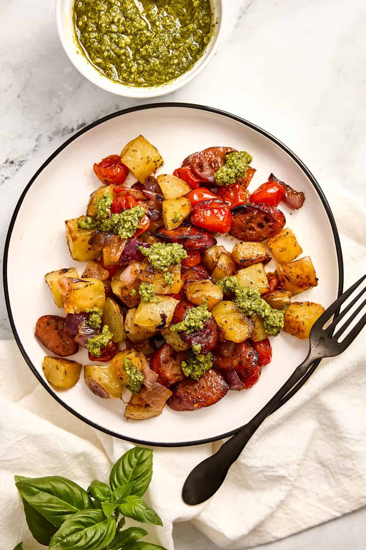 Chicken sausage sheet pan with vegetables and pesto on a plate with a fork.
