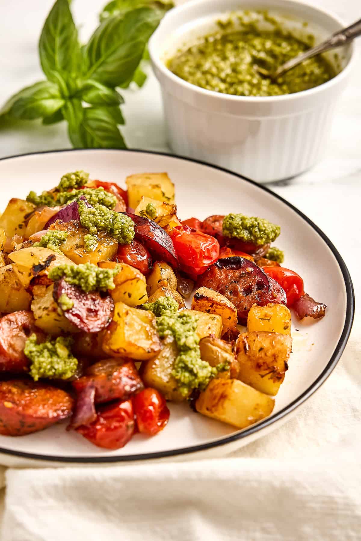 Chicken sausage, roasted vegetables, and dollops of pesto on a plate in front of pesto.