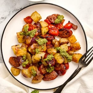 Chicken sausage sheet pan with vegetables and pesto on a plate with a fork.