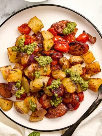 Chicken sausage sheet pan with vegetables and pesto on a plate with a fork.