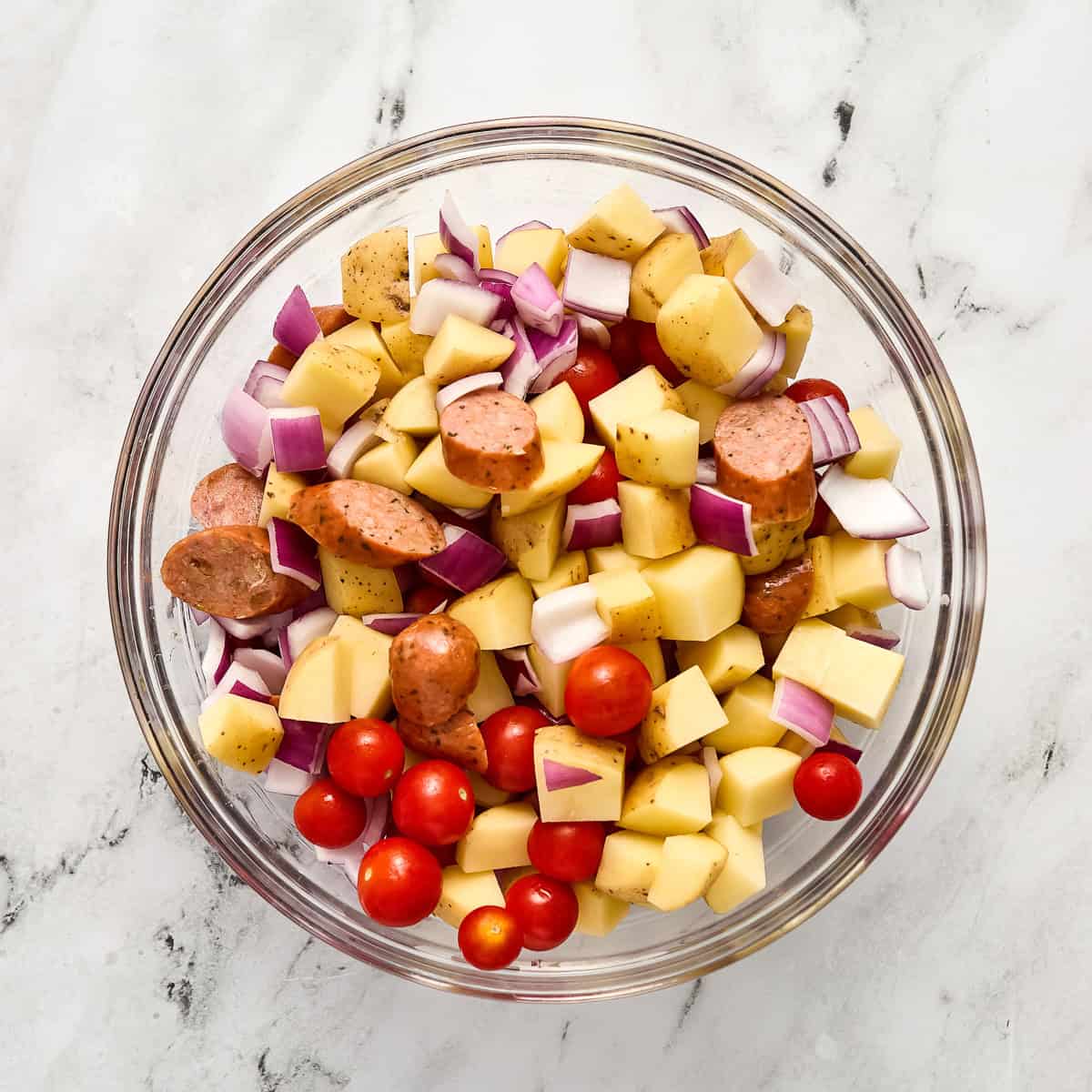 Sliced chicken sausage and chopped vegetables in a glass mixing bowl on a counter.