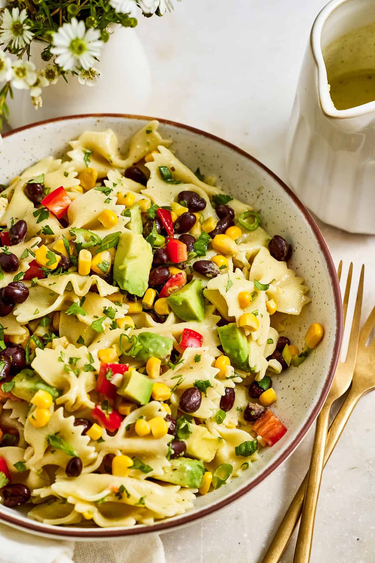 Pasta salad with lime dressing, avocado, beans, corns, and peppers in a bowl.
