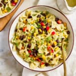 Southwest pasta salad in a bowl on a napkin with a spoon next to dressing.