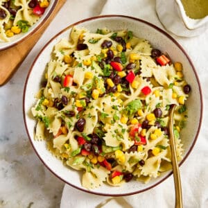 Southwest pasta salad in a bowl on a napkin with a spoon next to dressing.