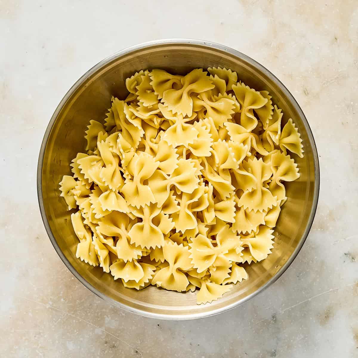 Cooked bowtie pasta in a large mixing bowl on a counter.