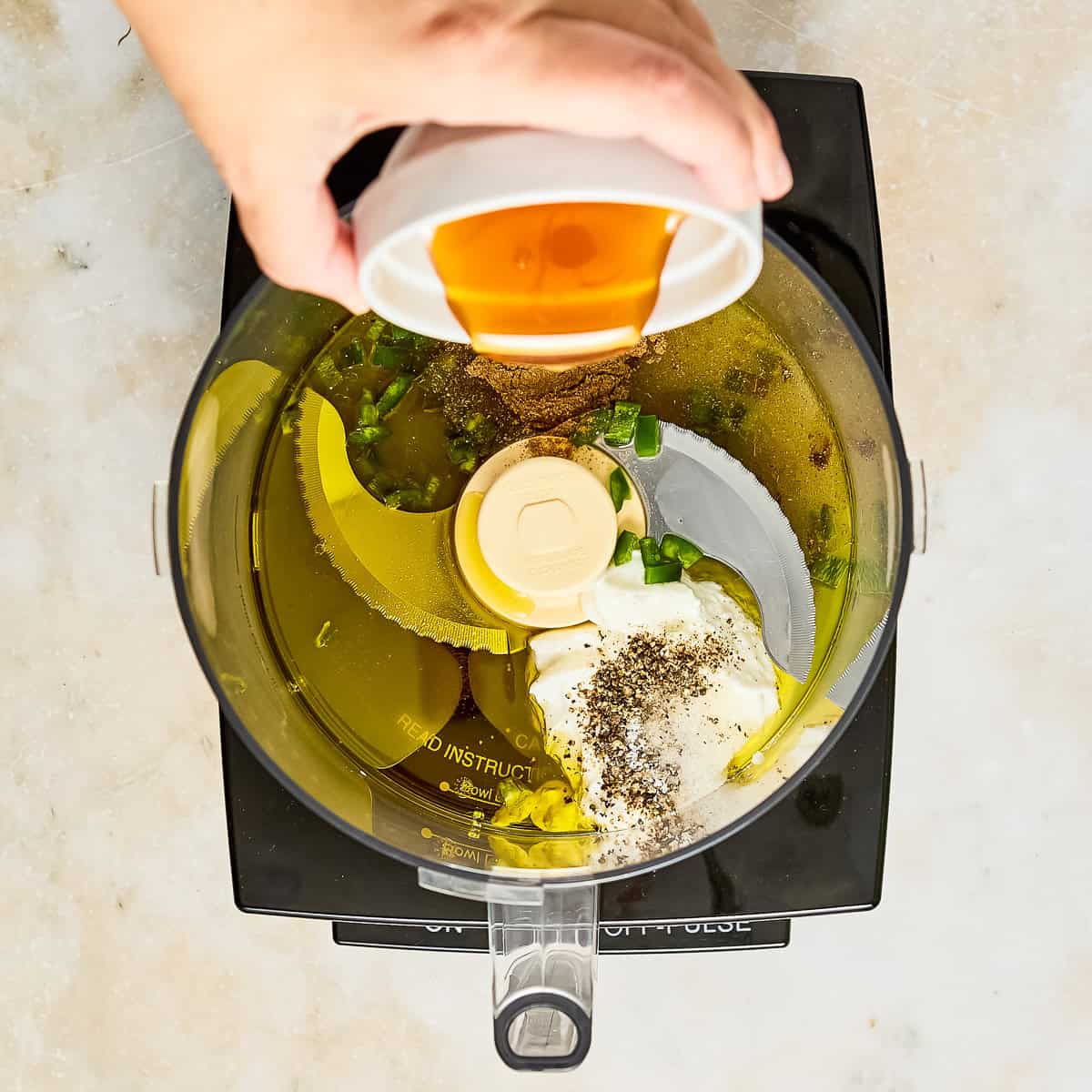 Woman pouring honey into a food processor with ingredients for salad dressing.