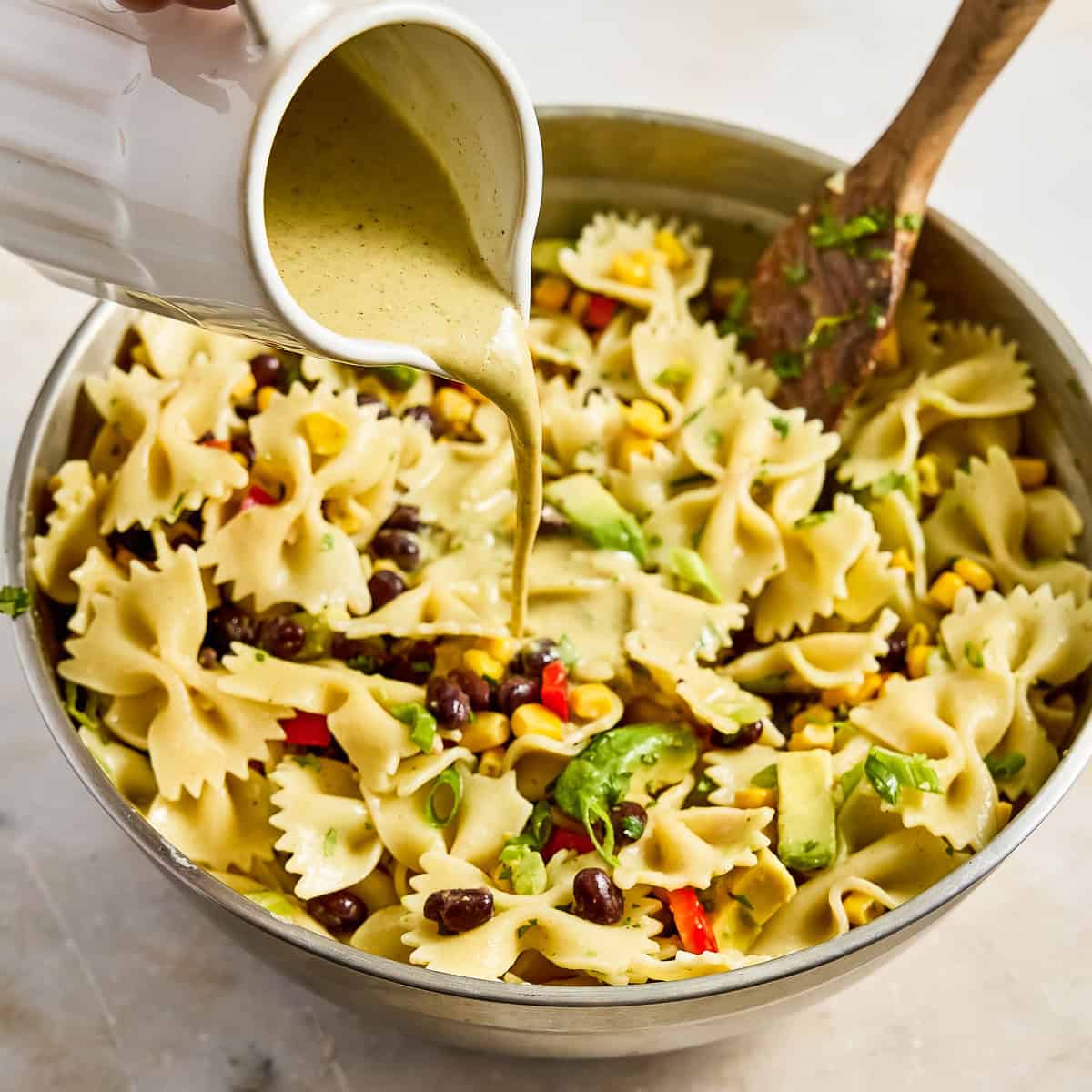 Dressing being poured from a pitcher onto Southwest pasta salad in a bowl.