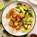 Sticky tofu with rice and cucumber salad surrounded by ingredients and toppings.