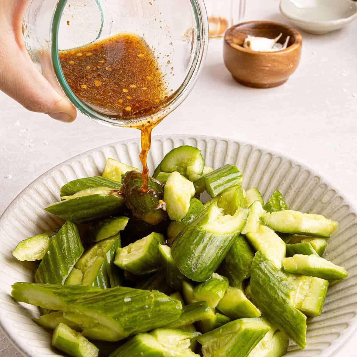 Woman pouring dressing over smashed cucumbers in a bowl.