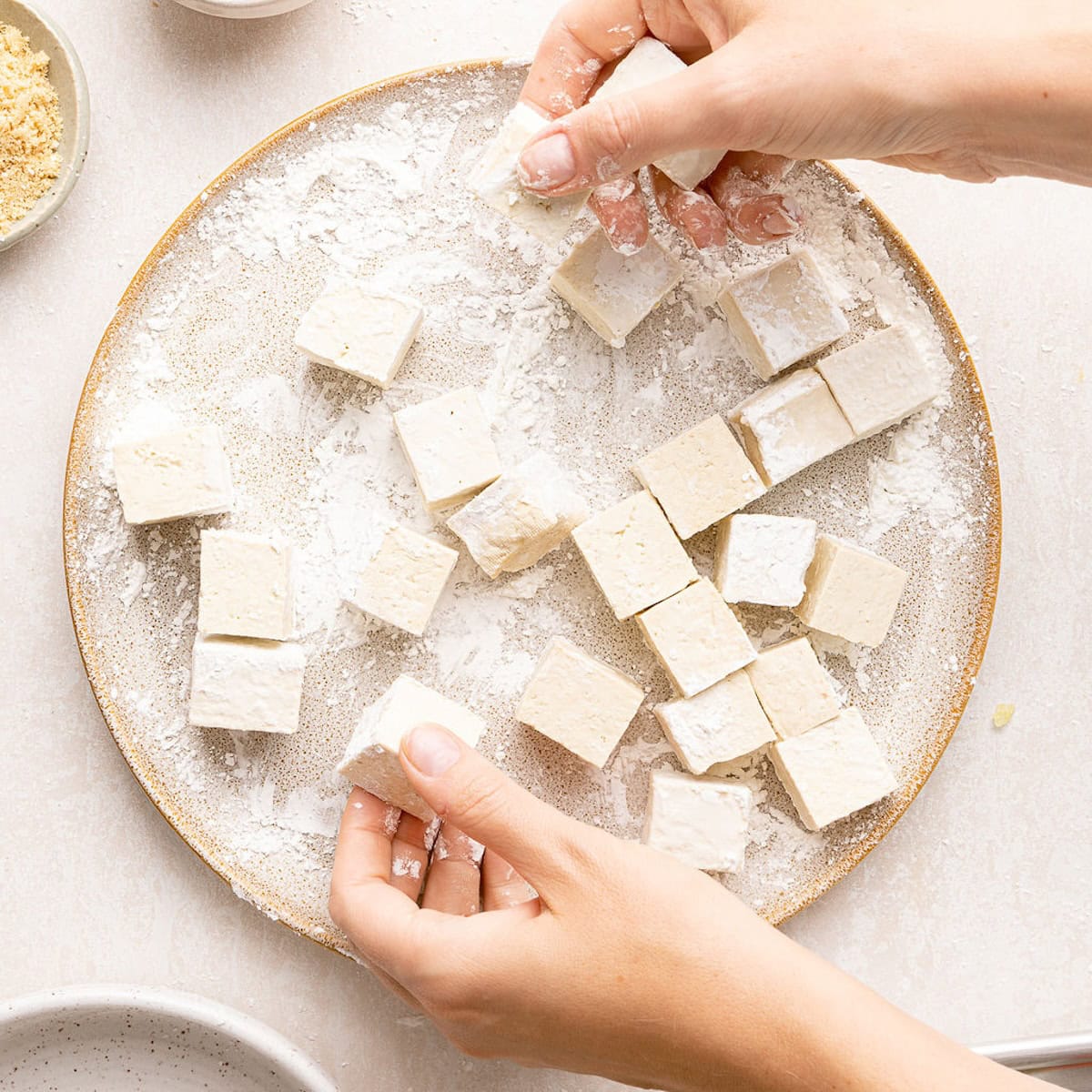 Woman tossing tofu cubes in cornstarch on a plate.