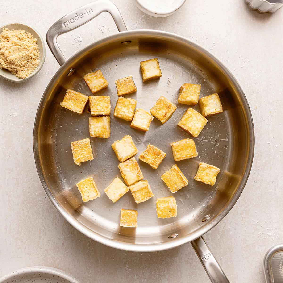 Crispy tofu cubes cooking in a skillet with oil.