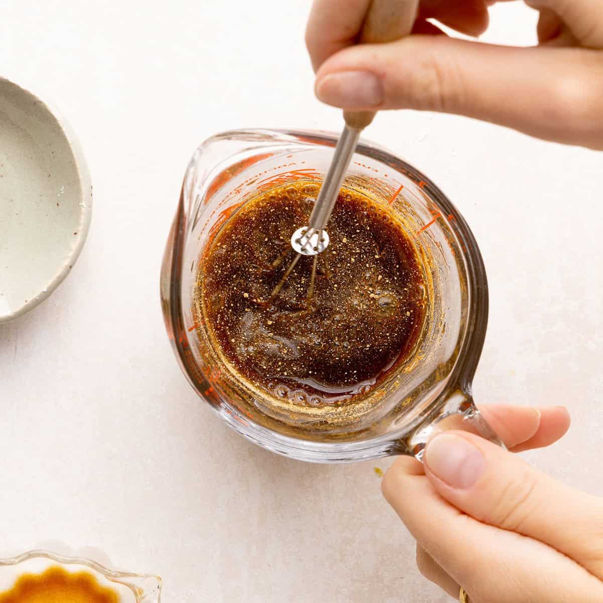 Woman whisking a soy sauce and brown sugar glaze for tofu in a measuring cup.