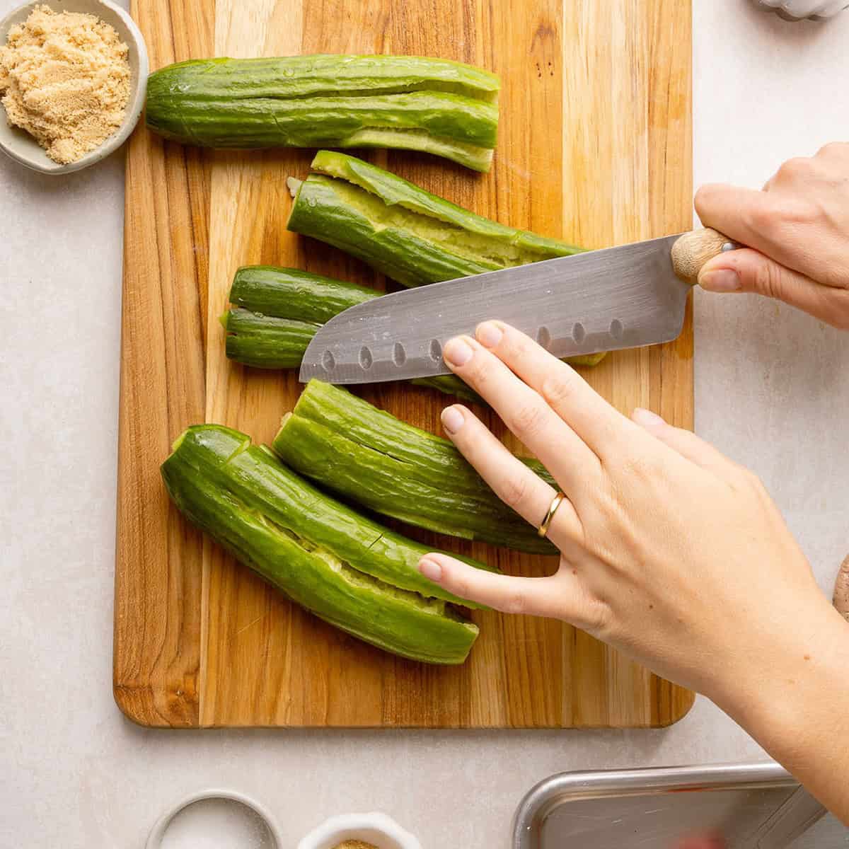 Woman smashing Persian cucumbers with the back of a chef's knife.