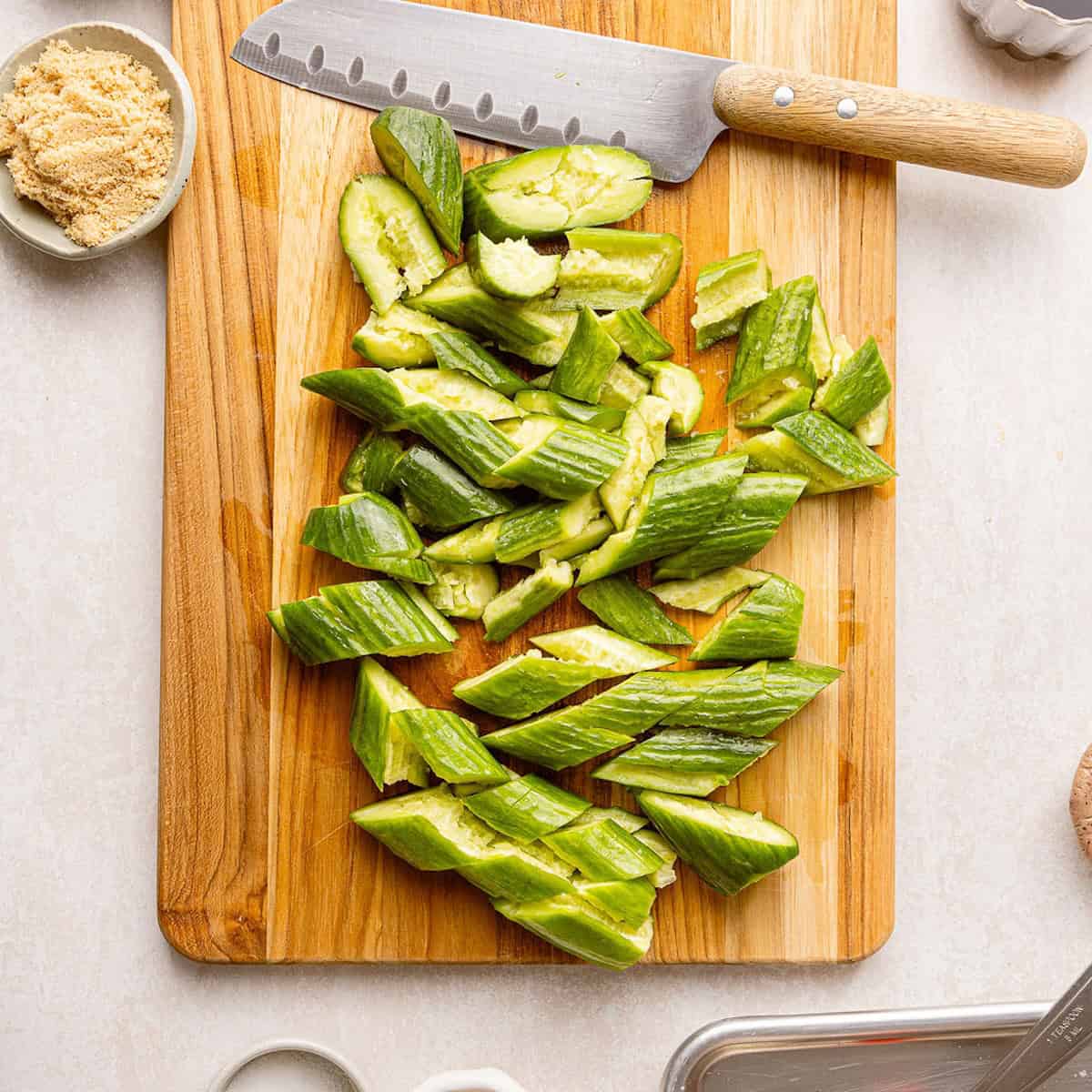 Smashed cucumbers sliced on a diagonal on a cutting board with a knife.