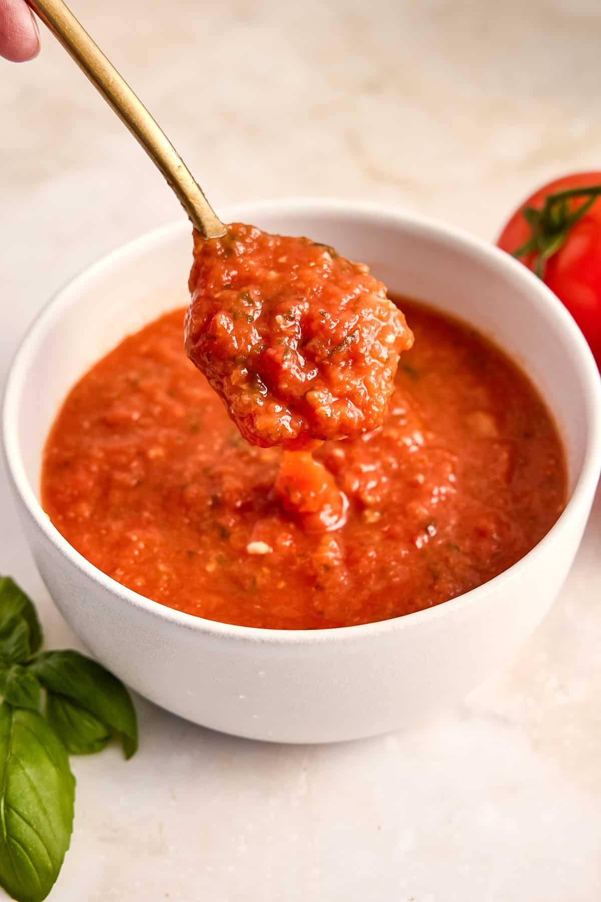 Woman lifting a spoon of fresh tomato sauce out of a bowl on a counter.