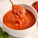Woman lifting a spoon of fresh tomato sauce out of a bowl on a counter.