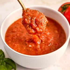 Woman lifting a spoon of fresh tomato sauce out of a bowl on a counter.