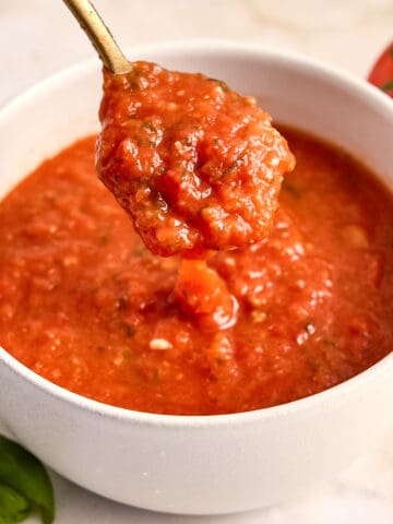 Woman lifting a spoon of fresh tomato sauce out of a bowl on a counter.