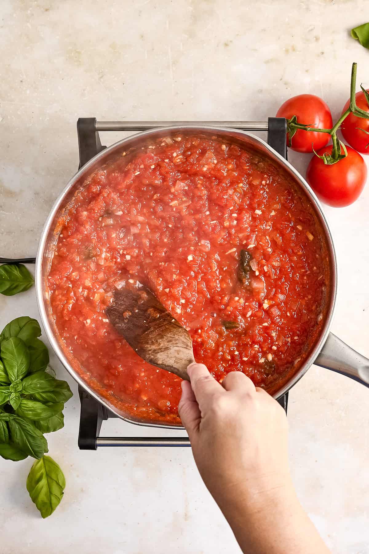 Woman stirring fresh tomato sauce after it cooked down in a saucepan.