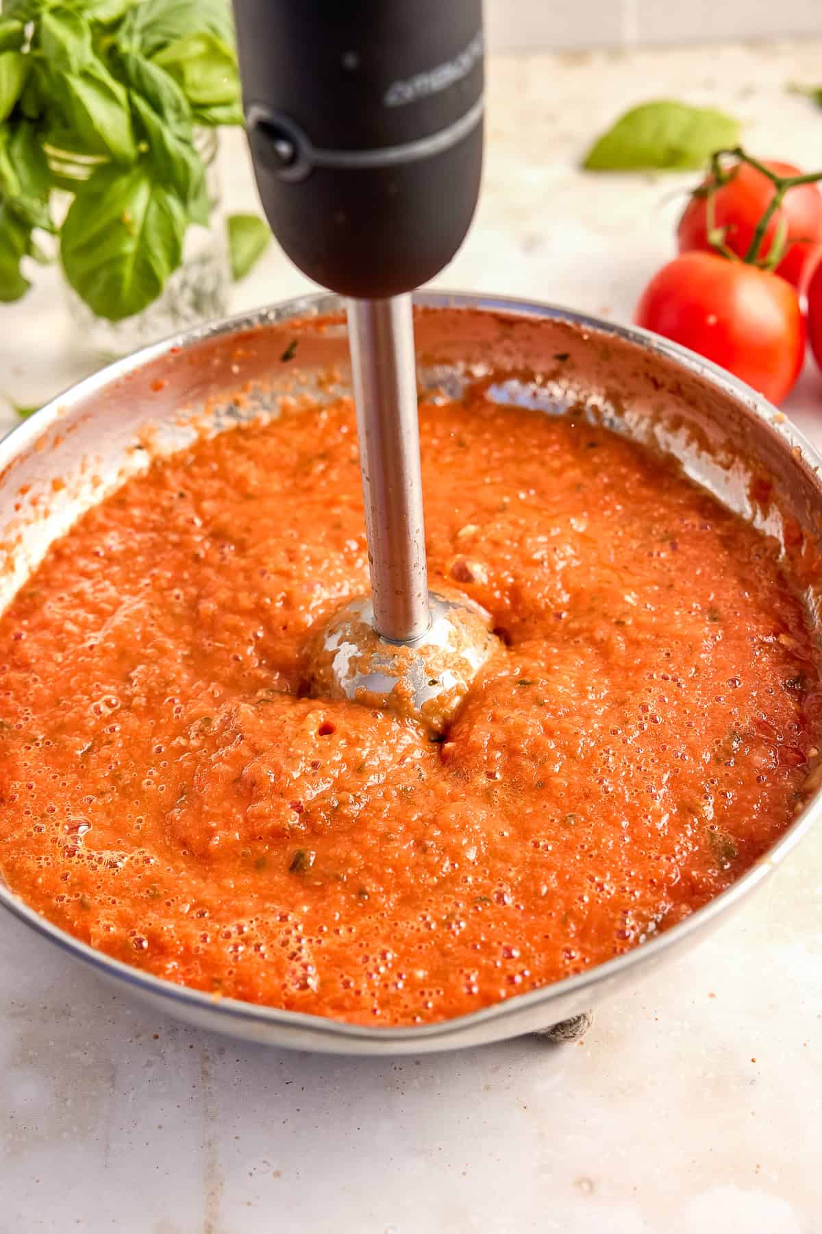 Woman blending homemade tomato sauce with a handheld blender in a saucepan.