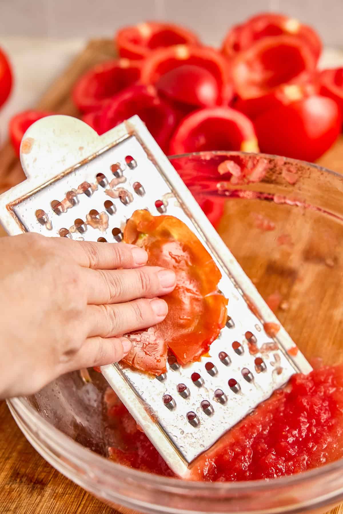 Woman grating tomato flesh away from the skin on a box grater in a bowl.