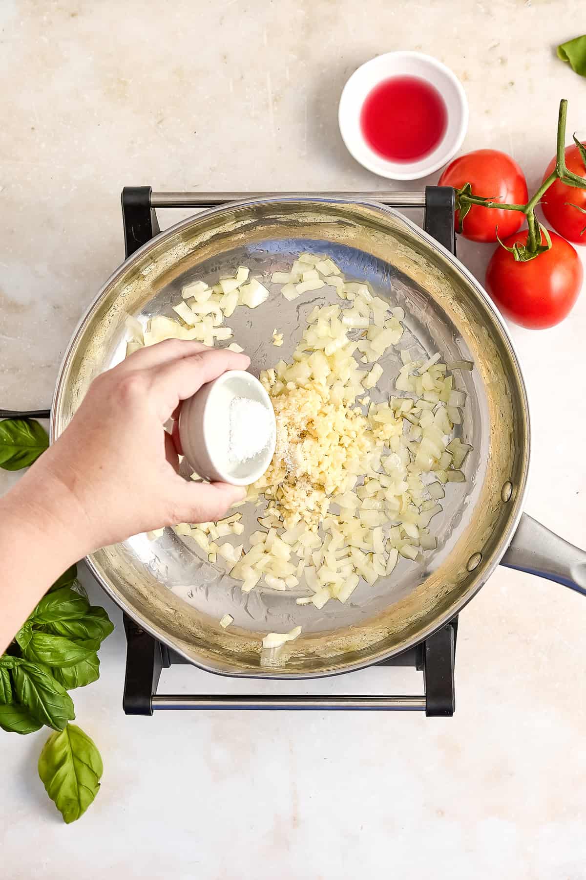 Woman adding salt to cooked onion and garlic in a saucepan.