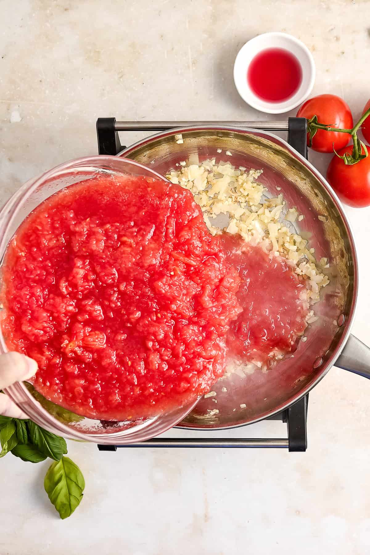 Woman adding tomato flesh to a saucepan with cooked onion and garlic.
