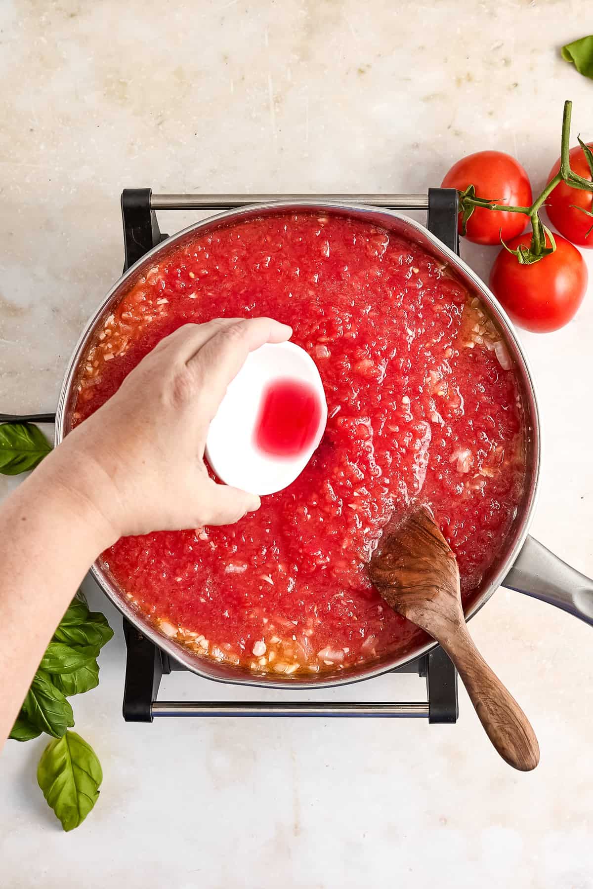 Woman adding red wine vinegar to fresh tomato sauce ingredients in a saucepan.