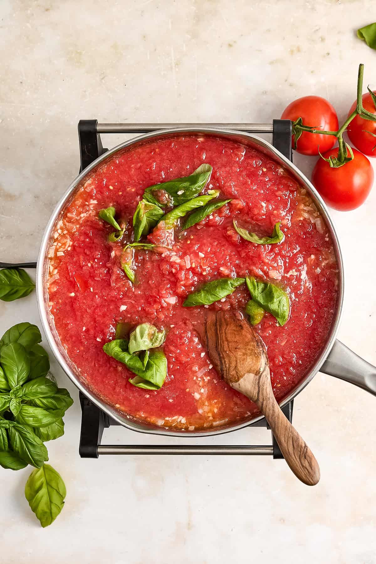 Basil leaves in fresh tomato flesh in a saucepan with a wooden spoon.