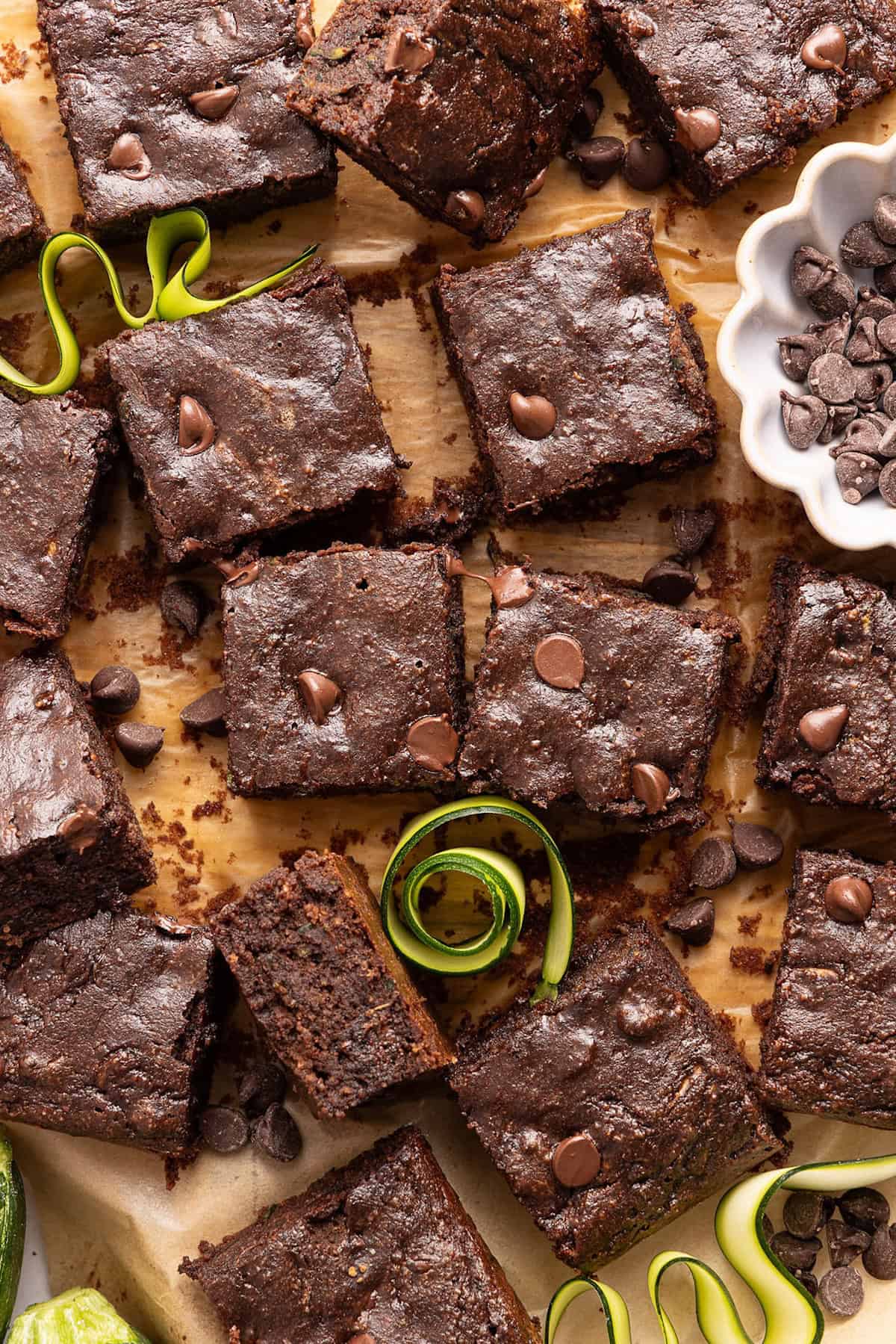 Zucchini brownies on a board next to zucchini swirls and chocolate chips.