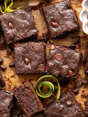 Zucchini brownies on a board next to zucchini swirls and chocolate chips.