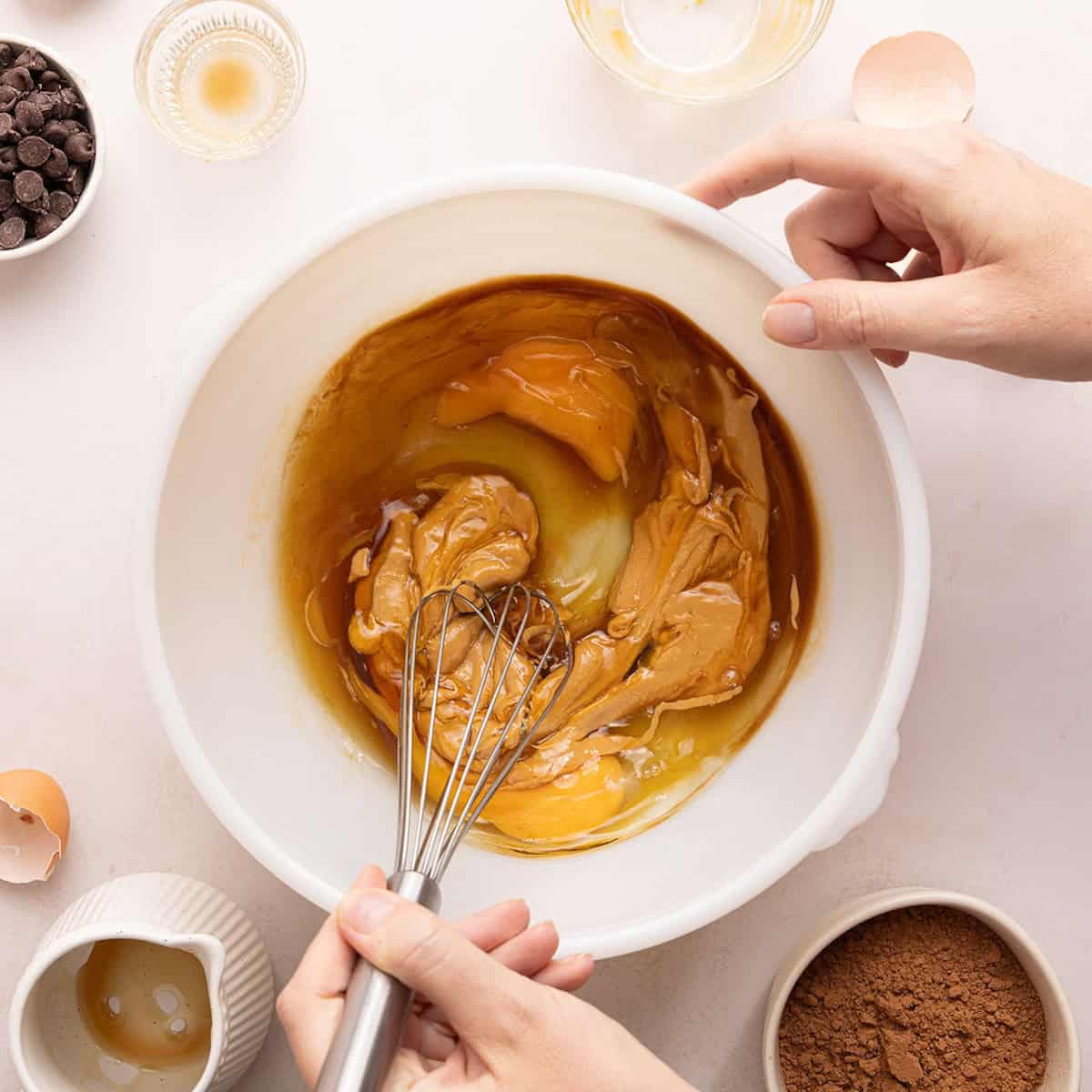 Woman whisking eggs with peanut butter, maple syrup, and vanilla extract in a bowl.