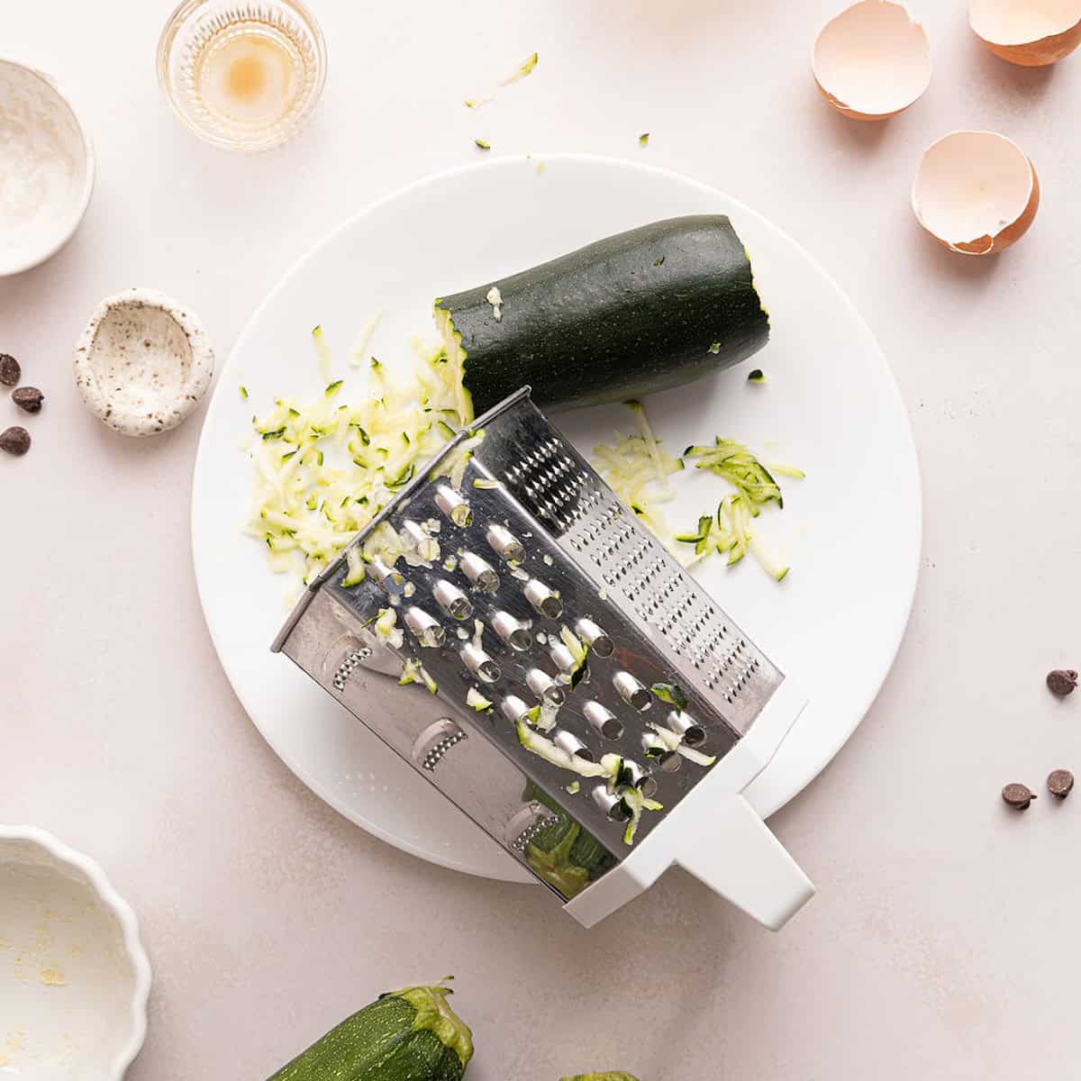 Grated zucchini on a plate next to the box grater used.