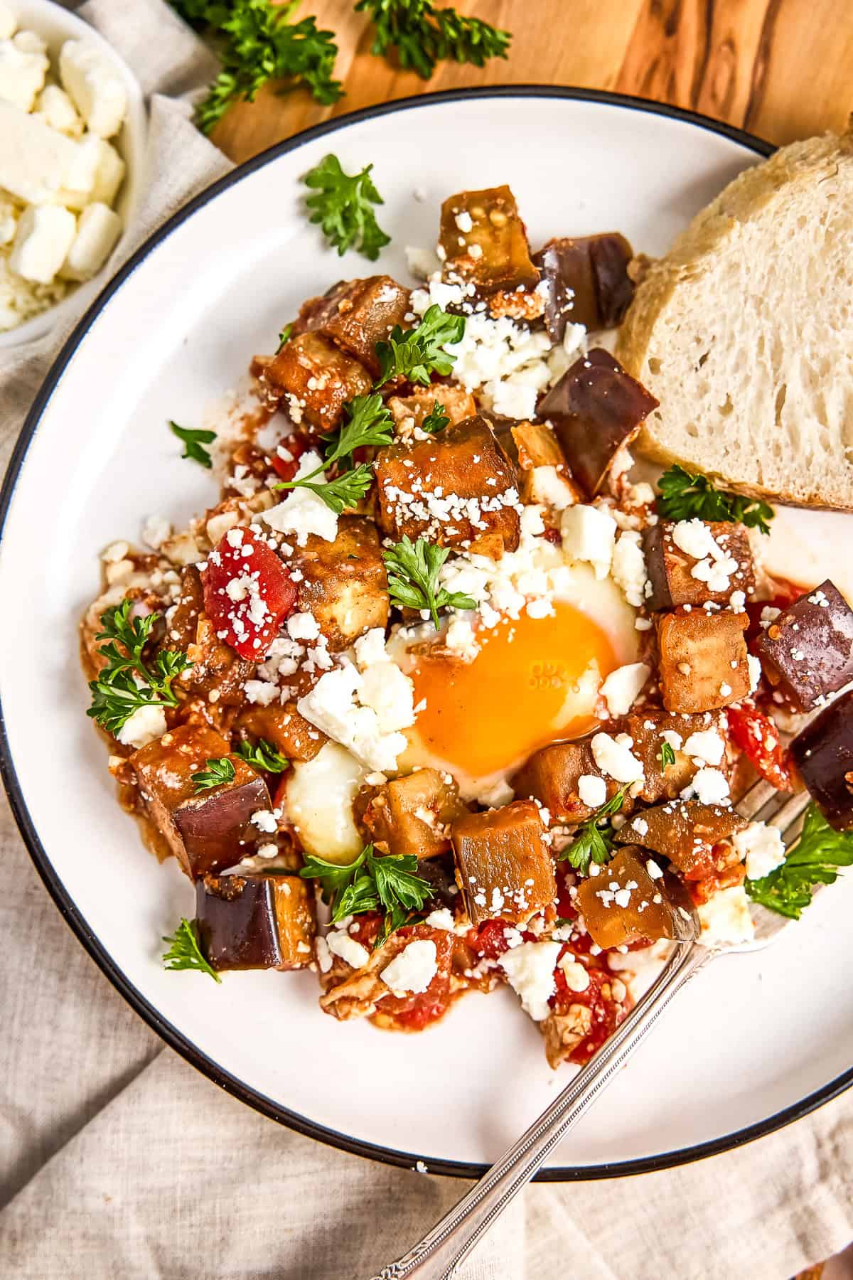 Plate of eggplant shakshuka with a poached egg and slice of bread.