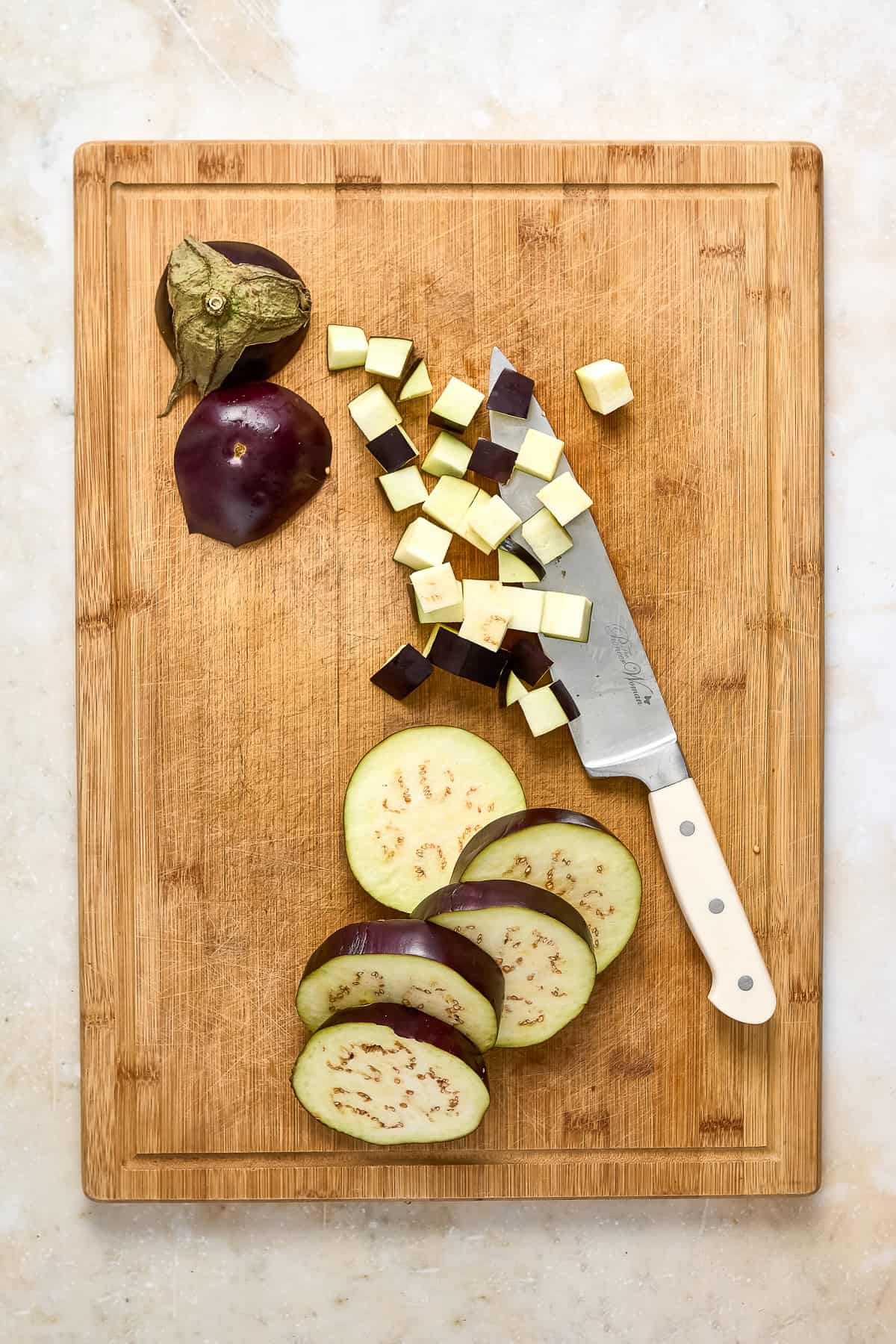 Eggplant diced into cubes on a cutting board with a knife.